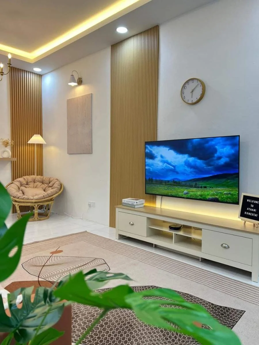 Ruang tamu Ayaani Homestay dengan TV, kerusi papasan dan pencahayaan hangat
